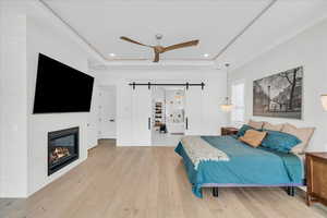 Bedroom featuring a barn door, light hardwood / wood-style floors, ceiling fan, and a tray ceiling