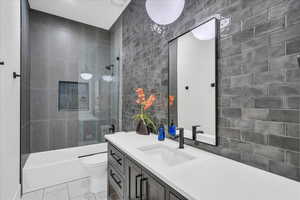 Full bathroom with vanity, toilet, tiled shower / bath, and tile walls