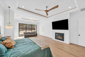 Bedroom featuring ceiling fan with notable chandelier, light wood-type flooring, access to exterior, and a raised ceiling