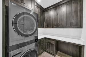 Clothes washing area with light hardwood / wood-style floors, cabinets, and stacked washing maching and dryer