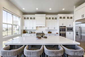 Kitchen featuring white cabinets, appliances with stainless steel finishes, a center island with sink, and premium range hood