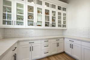 Kitchen with light stone counters, white cabinetry, light wood-type flooring, and tasteful backsplash