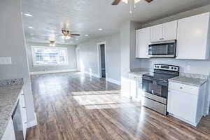 Kitchen with light stone countertops, white cabinetry, stainless steel appliances, and wood-type flooring