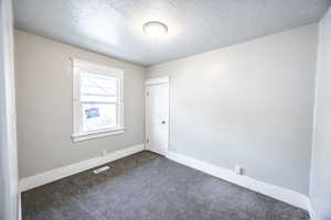 Unfurnished room featuring dark carpet and a textured ceiling