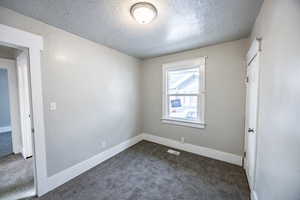 Spare room with dark carpet and a textured ceiling