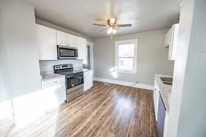 Kitchen featuring ceiling fan, light stone countertops, light hardwood / wood-style floors, white cabinets, and appliances with stainless steel finishes