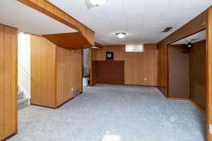 Basement family room featuring wooden walls and light carpet