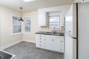 Kitchen with white cabinets, decorative light fixtures, white fridge, and sink