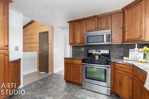 Kitchen featuring flooring, stainless steel appliances, backsplash, lofted ceiling, and wooden walls