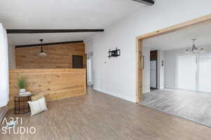 Interior space featuring a chandelier, vaulted ceiling with beams, wood-style flooring, and wooden walls