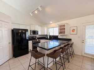 Kitchen featuring lofted ceiling, kitchen peninsula, appliances with stainless steel finishes, a kitchen bar, and white cabinetry