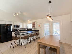 Kitchen with stainless steel appliances, vaulted ceiling, sink, white cabinets, and a breakfast bar area