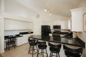 Kitchen with a breakfast bar, light tile patterned flooring, white cabinetry, and stainless steel appliances