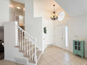 Entryway featuring light tile patterned floors, a textured ceiling, a high ceiling, and an inviting chandelier