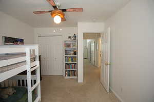 Bedroom with ceiling fan, a closet, light colored carpet, and a textured ceiling