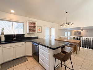 Kitchen featuring lofted ceiling, kitchen peninsula, sink, decorative light fixtures, and white cabinetry