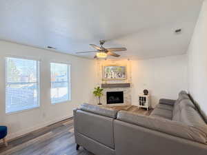 Living room featuring hardwood / wood-style floors, a large fireplace, a textured ceiling, and ceiling fan