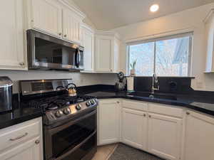 Kitchen with appliances with stainless steel finishes, vaulted ceiling, white cabinetry, and sink