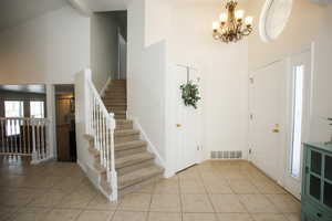 Foyer featuring light tile patterned flooring, beam ceiling, high vaulted ceiling, and a chandelier