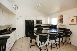 Kitchen with white cabinetry, stainless steel appliances, kitchen peninsula, lofted ceiling, and light tile patterned floors