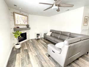 Living room featuring a tile fireplace, hardwood / wood-style floors, a textured ceiling, and ceiling fan