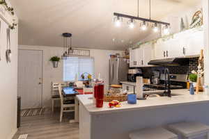 Kitchen featuring stainless steel appliances, wood-style flooring, kitchen peninsula, decorative light fixtures, and white cabinets