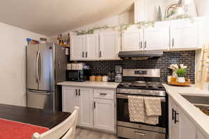 Kitchen featuring lofted ceiling, white cabinets, decorative backsplash, stainless steel appliances, and wood-style floors