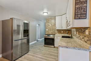 Kitchen with backsplash, light stone-like countertops, white cabinetry, stainless steel range and fridge are negotiable