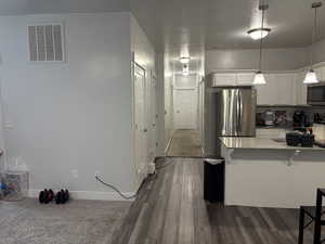 Kitchen with appliances with stainless steel finishes, dark hardwood / wood-style flooring, a breakfast bar, decorative light fixtures, and white cabinets