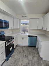 Kitchen featuring stainless steel appliances, white cabinetry, light hardwood / wood-style floors, and sink