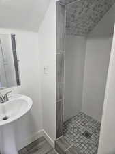 Bathroom featuring a textured ceiling, sink, wood-type flooring, and tiled shower