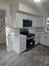 Kitchen with white cabinetry, a textured ceiling, and black range with electric cooktop