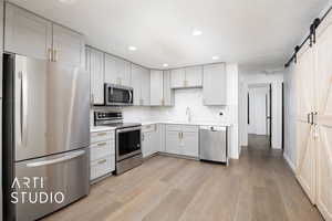 Kitchen with light wood-type flooring, stainless steel appliances, sink, a barn door, and white cabinets