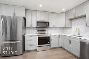 Kitchen with a textured ceiling, stainless steel appliances, light hardwood / wood-style flooring, and sink