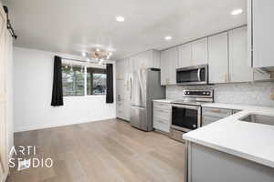 Kitchen featuring a barn door, light wood-type flooring, a textured ceiling, appliances with stainless steel finishes, and white cabinetry