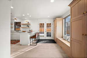 Kitchen featuring light brown cabinetry, french doors, light tile patterned floors, white cabinetry, and a breakfast bar area