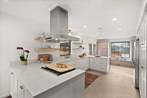 Kitchen with kitchen peninsula, light stone counters, island range hood, white cabinets, and stainless steel refrigerator