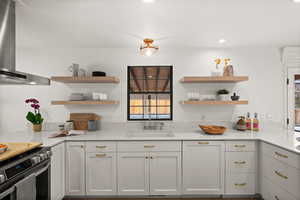 Kitchen with light stone countertops, stainless steel range, wall chimney exhaust hood, sink, and white cabinets