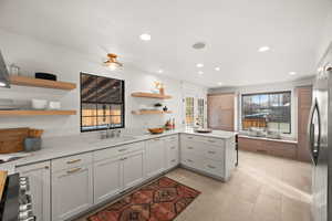 Kitchen featuring white cabinets, sink, stainless steel fridge, light tile patterned floors, and kitchen peninsula