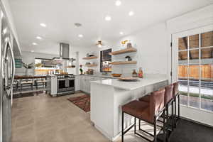 Kitchen with a kitchen bar, appliances with stainless steel finishes, kitchen peninsula, island range hood, and white cabinets