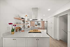 Kitchen featuring kitchen peninsula, island range hood, white cabinetry, and stainless steel refrigerator