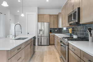 Kitchen with pendant lighting, sink, light wood-type flooring, an island with sink, and appliances with stainless steel finishes