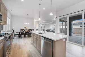 Kitchen featuring sink, hanging light fixtures, an island with sink, light hardwood / wood-style floors, and stainless steel appliances