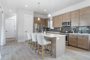 Kitchen featuring pendant lighting, sink, light hardwood / wood-style flooring, an island with sink, and stainless steel appliances