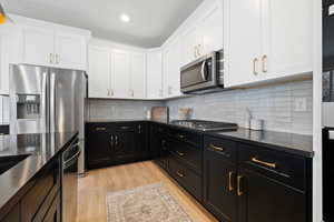 Kitchen with tasteful backsplash, white cabinetry, light wood-type flooring, and appliances with stainless steel finishes