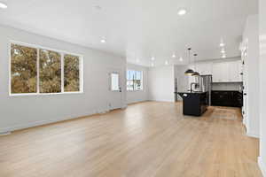 Kitchen featuring backsplash, sink, a center island with sink, light hardwood / wood-style flooring, and hanging light fixtures