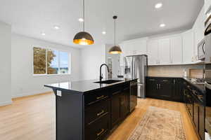 Kitchen featuring pendant lighting, a center island with sink, sink, white cabinetry, and stainless steel appliances