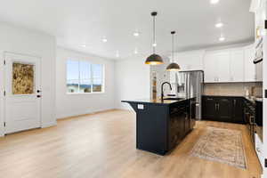 Kitchen with pendant lighting, a center island with sink, sink, decorative backsplash, and light wood-type flooring