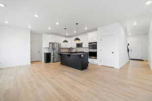 Kitchen featuring white cabinetry, a kitchen breakfast bar, light hardwood / wood-style floors, a kitchen island with sink, and appliances with stainless steel finishes