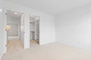 Unfurnished bedroom featuring a spacious closet, light carpet, and a closet